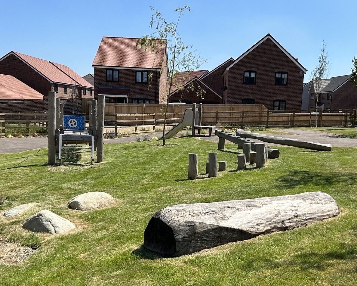 Natural play area at Bellway Homes, Eastern Counties, Stilton Gate, featuring glacial boulders and fallen logs and play panel